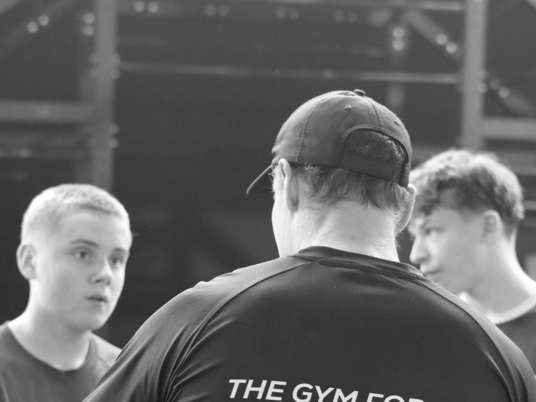 Bryan back to camera coaching young athletes inside the Nth Degree gym; 'Gym for Athletes' shirt visible.