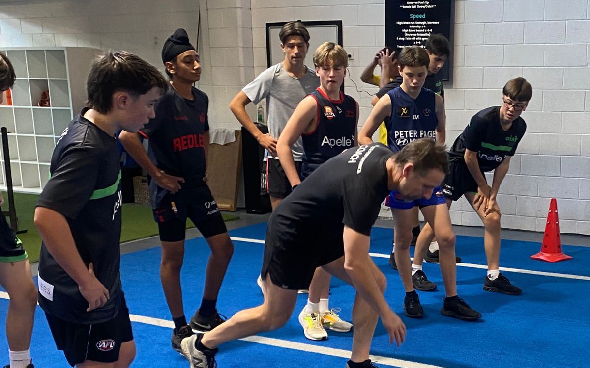 A coach demonstrating a warm-up drill to a group of athletes on the turf.
