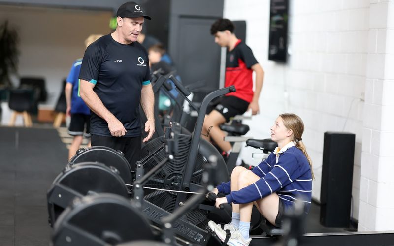 A coach standing beside an athlete on the bike, talking her through the effort.