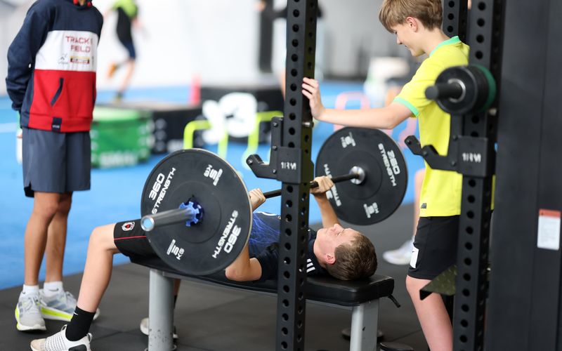 An athlete bench pressing while a teammate spots at the head of the bench.